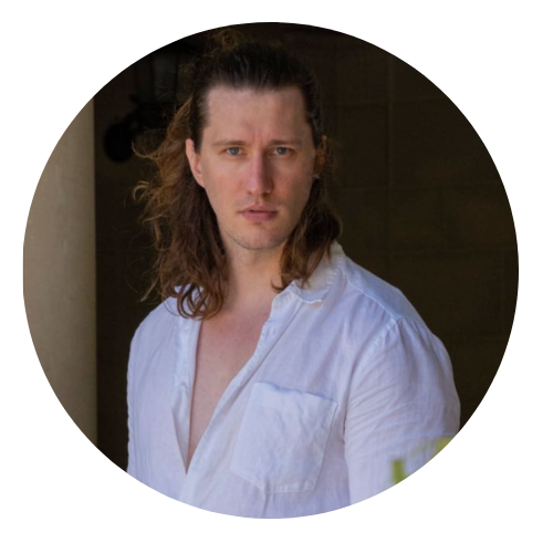 Male interior designer with long hair wearing a white shirt against a dark background