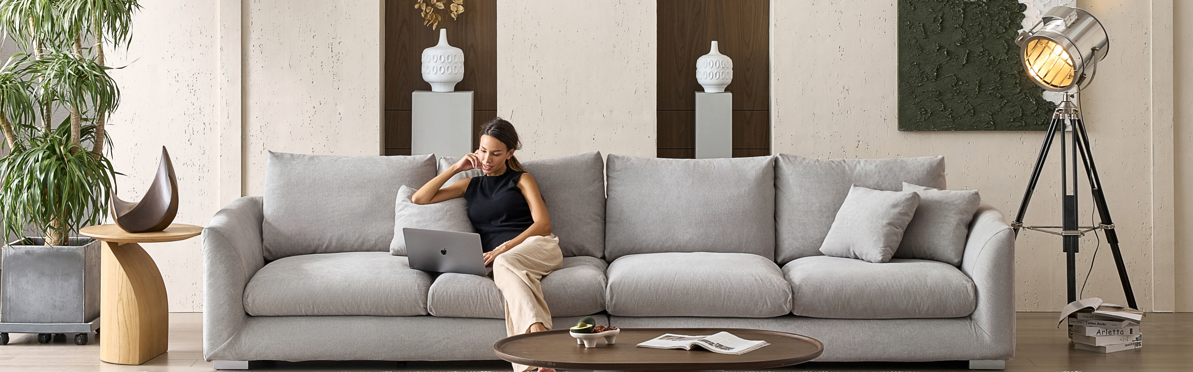 Woman in her living room with brutalist interior as she sits on a gray oversized extra deep sofa