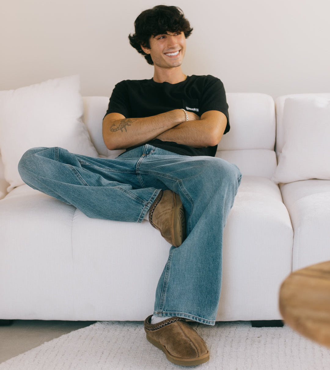Person sitting on a white couch wearing a black t-shirt and blue jeans.