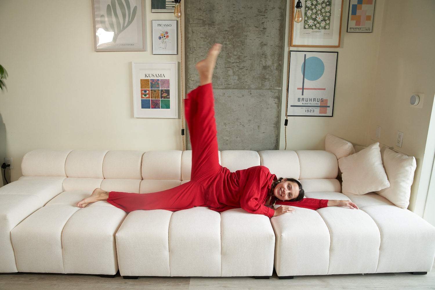 Person in a red outfit lying on a white couch with framed pictures on the wall.