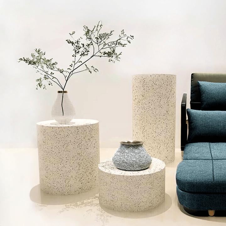 Accent side table in speckled stone paired with blue sectionals in a minimalist interior.